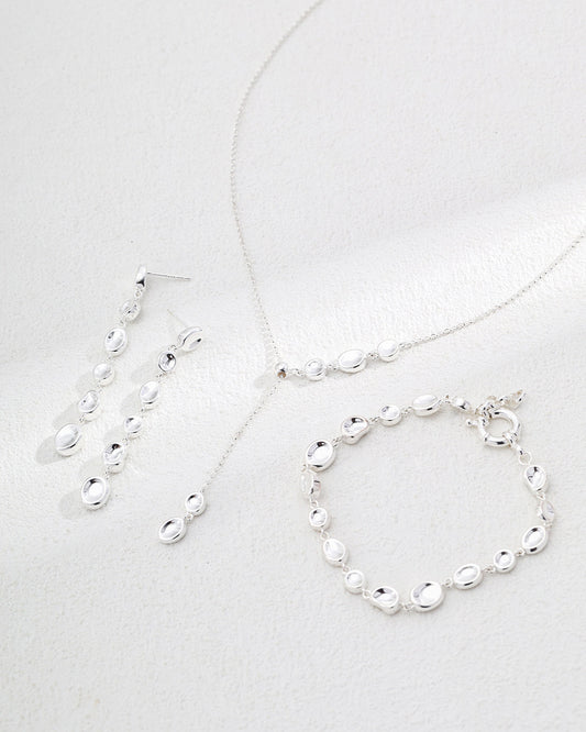 Silver jewelry set including necklace, bracelet, and earrings on a light gray background